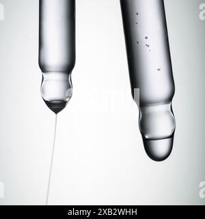 Un'immagine ravvicinata che cattura il momento delicato una goccia di liquido trasparente viene rilasciata dalla punta di un'elegante pipetta cosmetica contro uno sfondo neutro Foto Stock