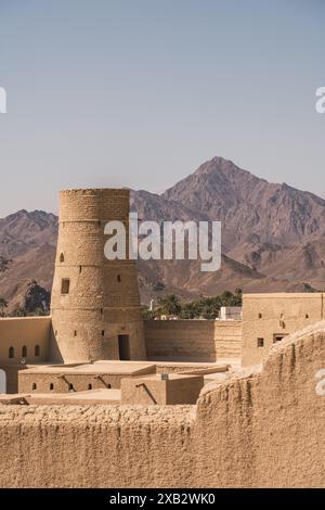 Un tradizionale forte Oman fatto di mattoni di argilla essiccati al sole si erge maestosamente con le aspre montagne di al Hajar sullo sfondo, catturando l'essenza Foto Stock