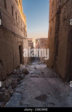 Un vicolo intempestivo corre tra le tradizionali case in mattoni di fango in un vecchio villaggio dell'Oman, catturando l'essenza rurale dell'Oman durante un tramonto dorato Foto Stock