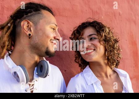 Una giovane coppia gode di una conversazione sentita contro un vivace muro rosa entrambi sorridono, catturando un momento di autentica connessione e felicità Foto Stock