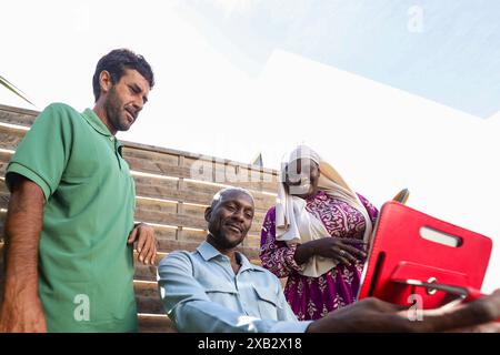 Un gruppo multietnico gode di una colazione all'aperto in un ambiente estivo, con una persona che usa un tablet Foto Stock