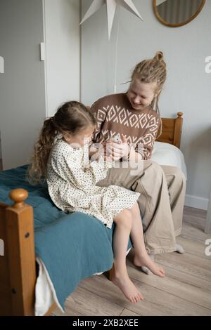 Una madre e una figlia sorridenti, comodamente sedute su un letto, condividono un momento di tenerezza tenendo delicatamente in mano un criceto. Entrambi guardano in basso la loro F. Foto Stock
