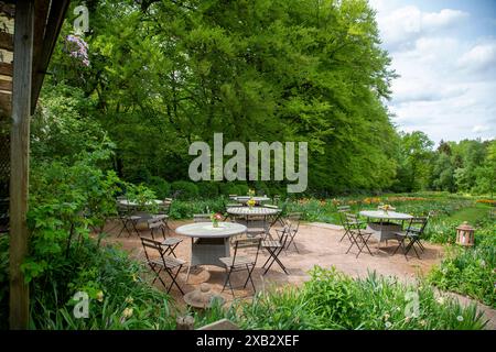 Invitante area caffetteria all'aperto con tavoli e sedie vuoti in ferro battuto circondata da una vegetazione vibrante e fiori in fiore in un tranquillo setti di fattoria Foto Stock