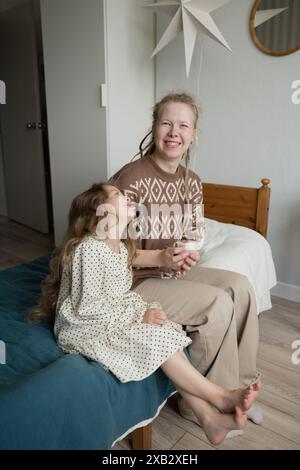 Una madre e una figlia allegra sedute su un letto a casa, sorridono e guardano la telecamera, mentre giocano con un criceto. Foto Stock
