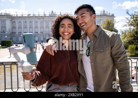 Una coppia multietnica sorridente, composta da un uomo cinese e una donna ispanica, si fa un selfie di fronte a un edificio storico di Madrid, in Spagna. Loro Foto Stock