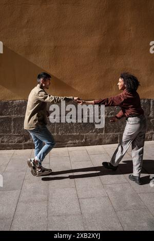 Una coppia multietnica composta da un uomo cinese e una donna ispanica che si diverte e si tengono per mano mentre cammina in una giornata di sole a Madrid, in Spagna. Il li Foto Stock