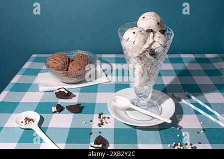 Elegante bicchiere ripieno di biscotti e gelato, accompagnato da una ciotola di sessole di cioccolato, su una tovaglia a scacchi blu con co sparso Foto Stock
