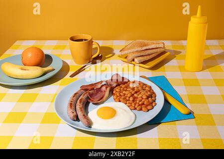 Tovaglia di colore giallo e sfondo con una deliziosa colazione all'inglese completa, uova, fagioli, salsicce e pancetta, fette di pane tostato, frutta e Foto Stock