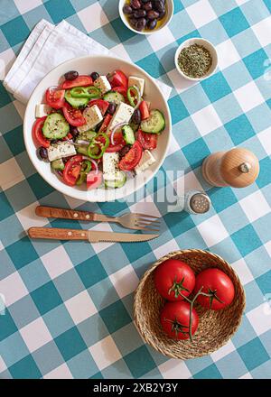 Una vivace insalata greca, disposta in una ciotola bianca su una tovaglia a scacchi blu e bianca, completa di pomodori, cetrioli, feta e olive, a. Foto Stock