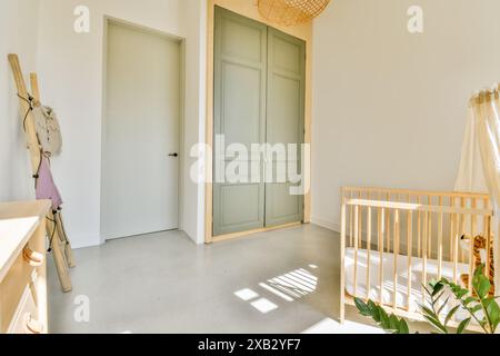 Una serena sala nursery che vanta un'ampia luce naturale, una culla in legno, colori tenui e interni dal design minimalista, offre un ambiente tranquillo e accogliente. Foto Stock