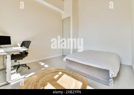 Uno spazio ufficio luminoso e moderno con scrivania bianca, sedia ergonomica e un comodo letto grigio, completato da un tappeto in tessuto naturale. Foto Stock