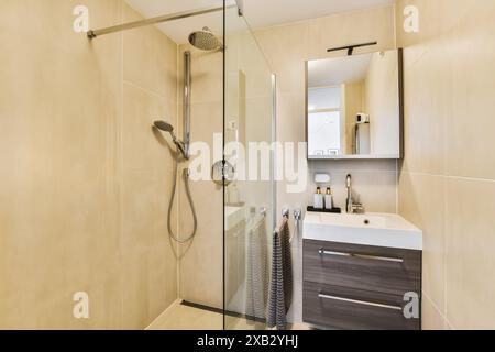 Un bagno contemporaneo presenta una doccia in vetro, piastrelle beige e un elegante piano lavabo su una tavolozza di colori neutri, creando uno spazio pulito e sereno Foto Stock