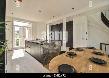 Cucina moderna spaziosa e ben illuminata con un'isola in marmo, tavolo da pranzo in legno per sei persone e tessuti misti che creano interni sofisticati. Foto Stock
