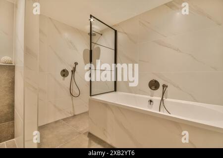 Un bagno elegante e contemporaneo con pareti in marmo lucido, box doccia in vetro, finiture eleganti e vasca bianca. Foto Stock