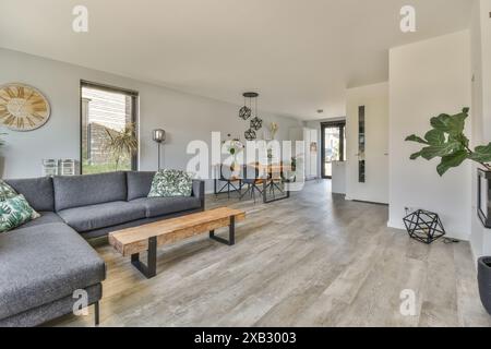 Un moderno soggiorno ben organizzato presenta un grande divano sezionale grigio, un tavolino da caffè in legno, lampade artistiche e una zona pranzo con un Foto Stock
