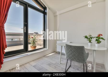 Moderna camera d'angolo con vista aperta sullo skyline urbano, con tende rosse luminose e un balcone con piante bianche e ariose, lo spazio include Foto Stock