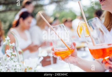 Bicchieri da primo piano con cannucce e aperol decorati con fette di arancio. Brindisi con bicchieri di bevanda alcolica agli agrumi. Le giovani donne si divertono a una festa. Foto Stock