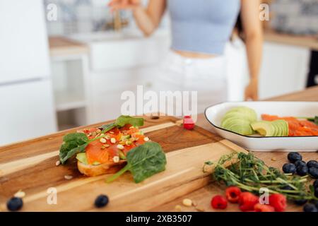 Primo piano di una deliziosa bruschetta con salmone, avocado, scialle e pinoli. Una giovane donna prepara una sana colazione in cucina a casa. Gustoso Foto Stock