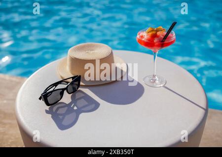 Una bevanda rossa in un elegante bicchiere con gambo lungo sul lato della piscina. Una bevanda alcolica di ghiaccio decorata con un fiore su uno sfondo di turchese Foto Stock
