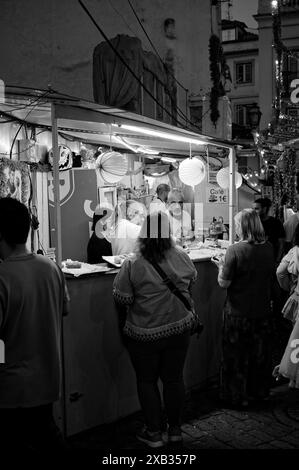 Le persone si riuniscono in una bancarella luminosa di cibo e bevande decorata con lanterne di carta colorata durante i popolari festeggiamenti dei Santi ad Alfama Foto Stock