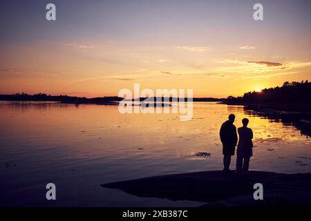 Vista posteriore della coppia in piedi sulla riva del lago contro il cielo durante il tramonto Foto Stock