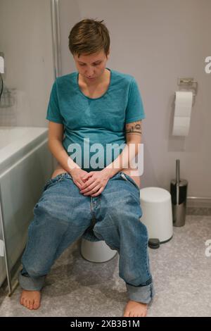 Foto a tutta lunghezza di una giovane donna incinta seduta sul sedile del water Foto Stock