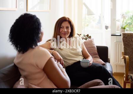Amiche mature che trascorrono il tempo libero sedendosi sul divano in soggiorno Foto Stock