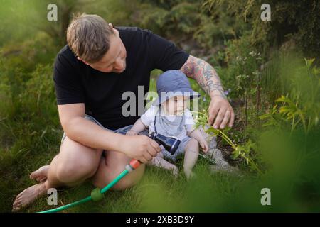 Papà spruzza acqua mentre siede con il bambino nel giardino sul retro Foto Stock