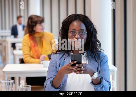 Ritratto di una donna d'affari sicura di sé che usa lo smartphone al tavolo della caffetteria dell'ufficio Foto Stock