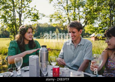 Giovane felice seduto in mezzo ad amici femminili mentre si godeva il solstizio d'estate nel cortile posteriore durante il brunch Foto Stock