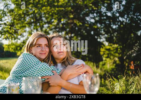 Una giovane donna sorridente che abbraccia un amico mentre si siede insieme nella giornata di sole Foto Stock