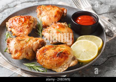 Cosce di pollo al limone al rosmarino al forno servite con ketchup da vicino in un piatto sul tavolo. Orizzontale Foto Stock