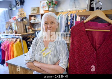 Ritratto di Volontario femminile Senior che lavora in Charity Shop o Thrift Store Vendita di abbigliamento usato e sostenibile Foto Stock