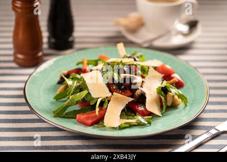 Insalata di verdure con rucola, pomodori ciliegini, funghi champignon fritti, basilico e fette di parmigiano su un piatto bianco in un ristorante sul Foto Stock