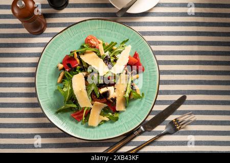 Insalata di verdure con rucola, pomodori ciliegini, funghi champignon fritti, basilico e fette di parmigiano su un piatto bianco in un ristorante sul Foto Stock