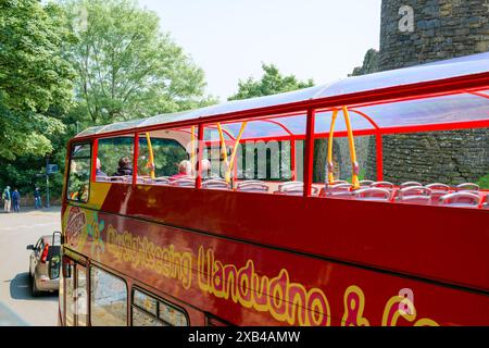 Conwy Wales Regno Unito 06-01-2024. Autobus rosso a due piani con i turisti che passano davanti a uno storico edificio in pietra in una giornata di sole Foto Stock