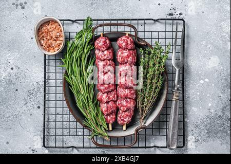 Kebab di Urfa Turco crudo decorato con erbe, spezie e forchetta di carne. Sfondo grigio. Vista dall'alto. Foto Stock