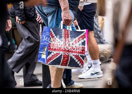 Uomo che cammina con una borsa di marca del rivenditore M&S Marks and Spencer Foto Stock