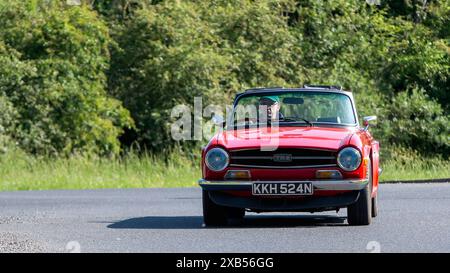 Stony Stratford, Regno Unito - 2 giugno 2024: 1975 auto d'epoca Triumph TR6 rossa su una strada di campagna britannica Foto Stock