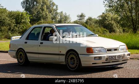 Stony Stratford, Regno Unito - 2 giugno 2024:1989 auto d'epoca bianca Ford Sierra Sapphire cosworth che guida su una strada di campagna britannica Foto Stock