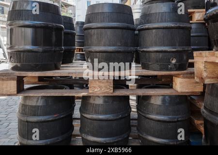 Una collezione di botti nere impilate ordinatamente su pallet in legno in un ambiente esterno. Foto Stock