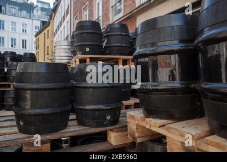 Una collezione di botti nere impilate ordinatamente su pallet in legno in un ambiente esterno. Foto Stock