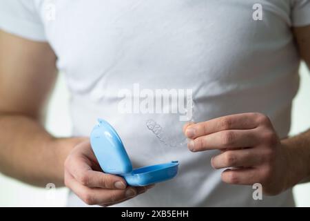 primo piano di un giovane che tiene in mano un fermo dentario invisibile e una custodia per la loro conservazione e protezione. Mani maschili che tengono l'allineatore dei denti dentali Foto Stock