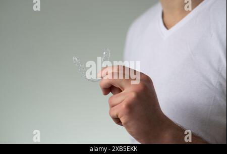 primo piano di un giovane che tiene in mano un fermo dentario invisibile e una custodia per la loro conservazione e protezione. Mani maschili che tengono l'allineatore dei denti dentali Foto Stock
