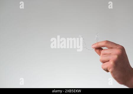 primo piano di un giovane che tiene in mano un fermo dentario invisibile e una custodia per la loro conservazione e protezione. Mani maschili che tengono l'allineatore dei denti dentali Foto Stock
