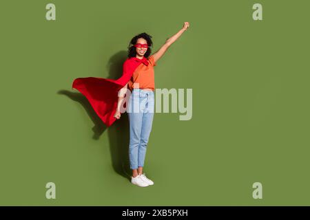 Foto a tutto il corpo di una giovane donna attraente che vola costume da supereroe vestito eleganti abiti arancioni isolati su sfondo color cachi Foto Stock