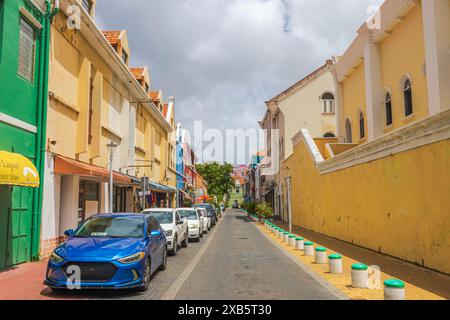 Splendida vista su una strada colorata con auto parcheggiate e architettura coloniale in una giornata di sole a Willemstad, Curacao. Foto Stock