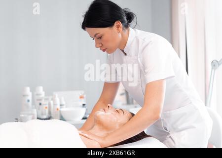 Cosmetologa donna in uniforme pulisce la pelle della donna con la schiuma. Procedura di cura della pelle femminile in una clinica di bellezza. Cosmetici naturali. Trattamento cosmetico della faccia. Crema peeling terapeutica. Foto Stock