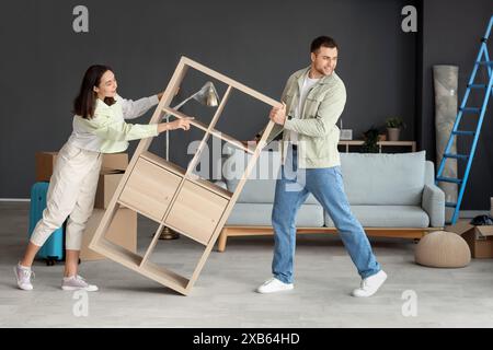 Felice giovane coppia che trasporta un ripiano in camera il giorno del trasloco Foto Stock