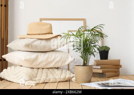 Pila di cuscini, cappello, impianto domestico e rivista su pallet di legno in camera da letto, primo piano Foto Stock